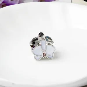 Detalle macro del charm de orquídea con esmalte blanco y gema rosa para pulseras DIY