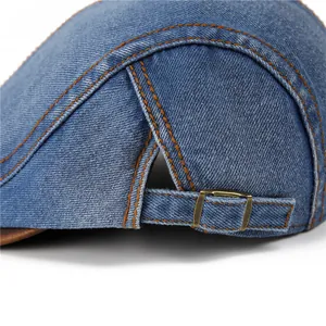 Detailed close-up of blue denim flat cap with orange contrast stitching and brass buckle