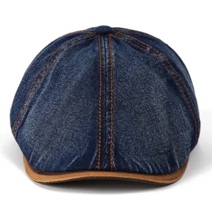 Detailed close-up of blue denim beret with orange stitching and brown leather-trimmed brim