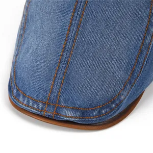 Detail of vintage denim cap showing orange contrast stitching and brown faux leather trim