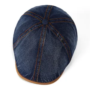 Top view of vintage blue denim beret with orange contrast stitching and leather brim