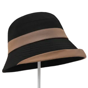 Detailed side view of black bucket hat with brown ribbon trim on a white display stand