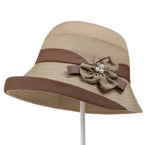 Detailed close-up of khaki sun hat with brown trim, fabric flower, and pearl accents