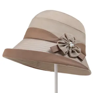 Detail of elegant beige cloche hat featuring decorative fabric flower and pearl accents