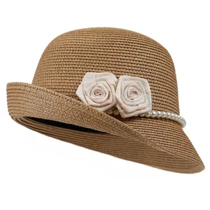 Close-up of brown straw sun hat featuring white fabric flowers and pearl accents