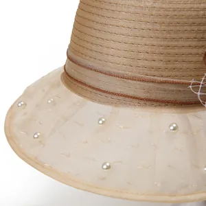 Détail d'un chapeau en paille kaki avec bord en organza et perles blanches élégantes