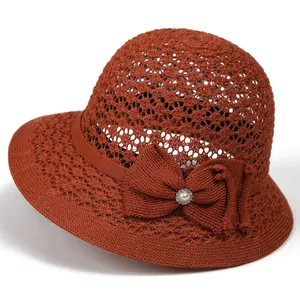 Detail of hand-woven brick red sun hat featuring a knit bow and elegant pearl accent