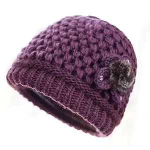 Detalle de gorro de invierno de punto morado oscuro con flor y pompón de piel sintética
