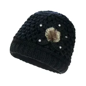 Detalle del gorro de punto negro con decoración floral y pompón de piel sintética