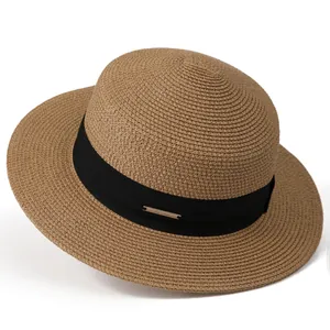 Detail of flat top straw hat featuring a black grosgrain ribbon and golden metal logo plate