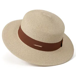 Macro detail of natural straw sun hat featuring brown ribbon and gold logo plaque