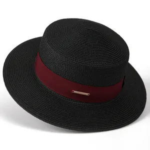 Detail of a black boater hat featuring a burgundy ribbon and gold logo metal plaque