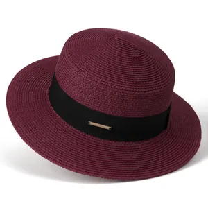 Detail of burgundy boater straw hat featuring a black ribbon and gold metal plaque