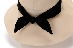 Close-up of beige sun hat featuring a black bow ribbon and precise stitching detail