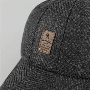 Detail van grijze visgraatstof en de bruine lederen merkpatch op de herenpet