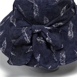Foldable navy sun hat with large bow and white feather pattern on textured fabric