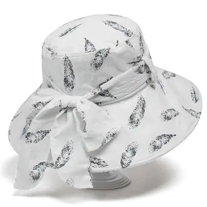 Detailed close-up of white summer sun hat with black feather prints and large bow accent