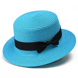 Detalle de sombrero de paja azul con copa plana y cinta negra sobre fondo blanco