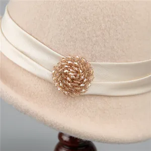 Beige wool cloche hat with satin ribbon and crystal beaded decoration on a wooden stand