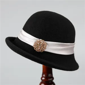 Detail of wool cloche hat featuring a pink satin ribbon and crystal brooch on wooden stand