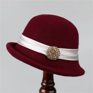Detail of burgundy wool felt cloche hat with white satin ribbon and gold crystal brooch