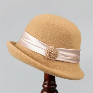 Detail of wool cloche hat with champagne satin ribbon and beaded brooch on wooden stand