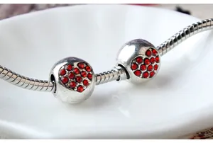 Bracelet serpent argenté avec breloques cœur en strass rouges sur assiette blanche en céramique