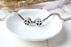 Silbernes Schlangenarmband mit Peace-Zeichen-Anhängern auf einer weißen Muschelschale