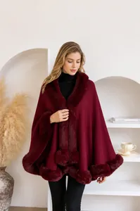 Close-up of wine red knit poncho featuring plush faux fur collar and pom-pom detail