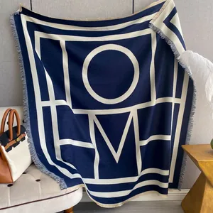 Detail of navy and beige knit shawl featuring 'HOME' lettering and decorative fringe edges