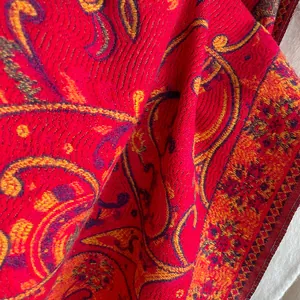 Gros plan du motif paisley rouge et or sur le tissu d'un châle d'hiver de qualité