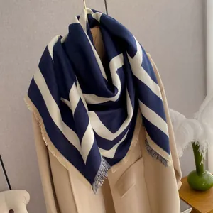 Detail of navy and beige geometric patterned scarf styled on a beige wool coat