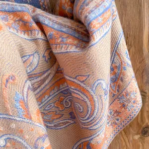Gros plan d'un châle à franges motif cachemire orange et bleu sur fond de bois naturel