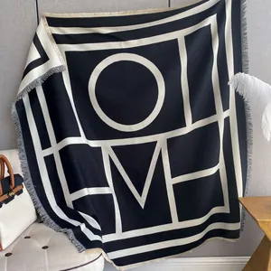 Modern black and white knit shawl featuring HOME lettering and fine tassel edges