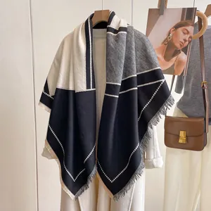 Detalle de bufanda geométrica suave con flecos sobre un abrigo blanco de moda