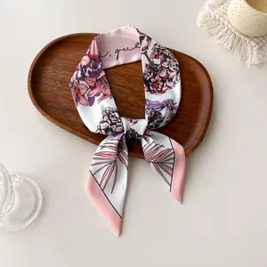 Close-up of a floral print twilly silk scarf with elegant pink lilies on a wood tray