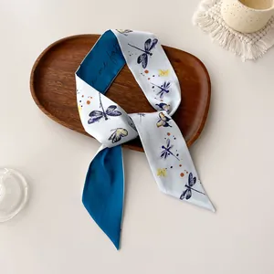 Macro detail of narrow silk twilly scarf with dragonfly prints on a wooden tray