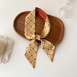 Detail van een gembergele lange twilly sjaal met wit raster en rode stippen op hout