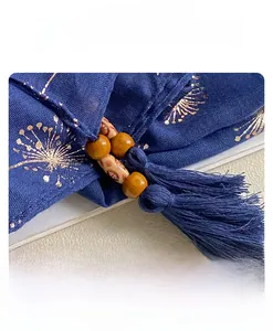 Close-up of navy blue linen scarf featuring golden dandelion prints and wooden bead tassels