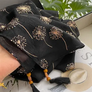 Detail of black cotton linen scarf featuring gold dandelion prints and wooden bead tassels
