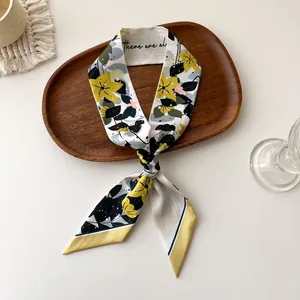 Détail d'un foulard étroit en soie à motif floral jaune noué sur un plateau en bois