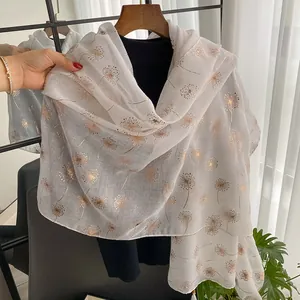 Elegant white floral scarf with gold dandelion patterns and fringe on a wooden hanger