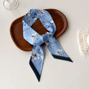 Detail of light blue floral skinny silk scarf with white lilies on a wooden tray