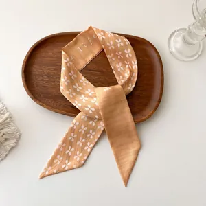 Détail d'un foulard en soie orange-rose avec motif floral et lettrage sur un plateau en bois