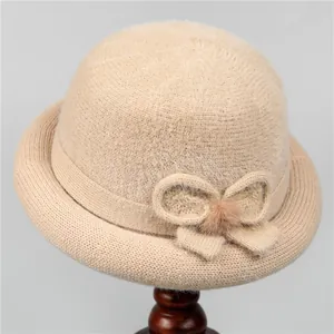 Close-up of beige knitted winter hat with decorative bow and soft fur ball detail