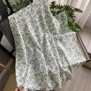 Elegant white cotton linen scarf with green leaf patterns and fringe hanging on a chair