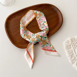 Detailweergave van zijden sjaal met oranje bloemenprint en ms dana letters ontwerp