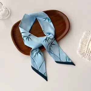 Detailed view of light blue twilly silk scarf with elegant green bamboo leaf prints