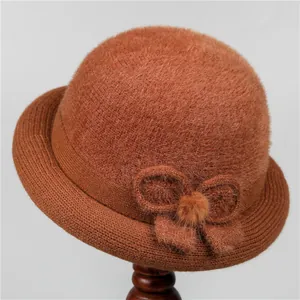 Close-up of brick red winter bucket hat with knitted bow and plush ball detail
