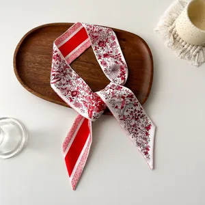 Détail d'un twilly en soie rouge à motifs floraux posé sur un plateau en bois
